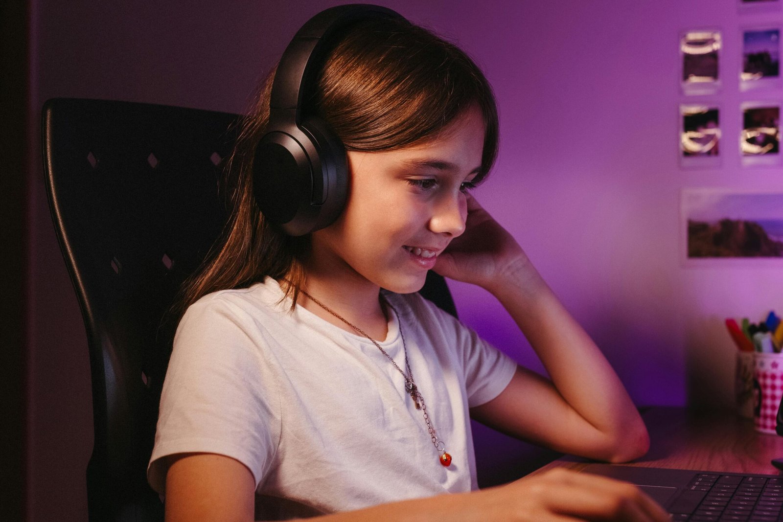 Young girl smiling while using a laptop and wearing headphones in a cozy indoor setting.