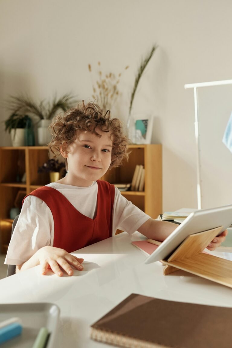 A cheerful boy in a red shirt studying on a tablet in a cozy home environment.